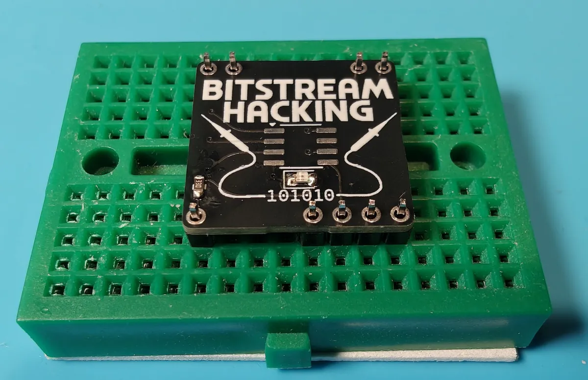 The minibadge sitting on header pins pushed into a green breadboard, pin tips poking through all nine holes
